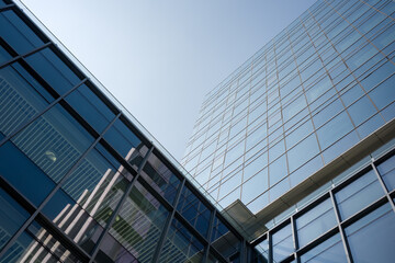 Obraz premium Modern glass curtain wall building captured from a low angle仰拍 perspective against clear blue sky