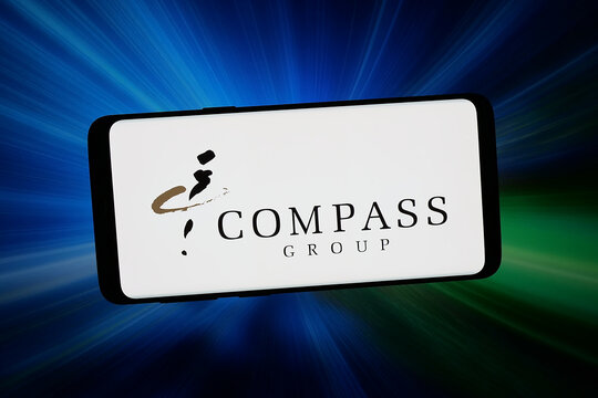 Stuttgart, Germany - 02-11-2026: In this photo illustration, the logo of British foodservice company Compass Group plc is displayed on a smartphone in front of abstract background on computer screen.