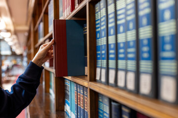 Hand selecting book from wooden library shelf. Legal research concept, attorney reference material, system study, academic knowledge and professional legislation archive. © Smallroombigdream