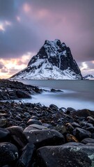 Snowy peak island rising from blurred ocean, foreground is rocks and sky is cloudy