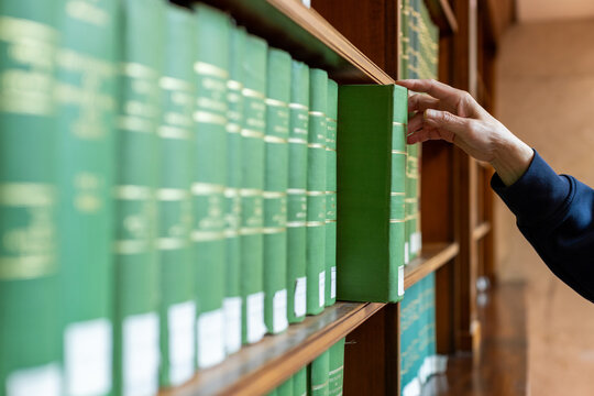 Hand selecting book from wooden library shelf. Legal research concept, attorney reference material, system study, academic knowledge and professional legislation archive.
