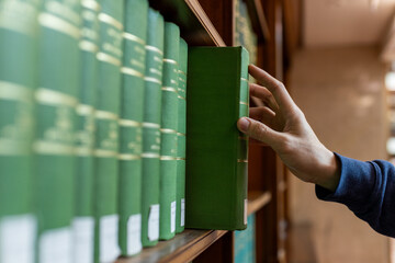 Hand selecting book from wooden library shelf. Legal research concept, attorney reference material, system study, academic knowledge and professional legislation archive. © Smallroombigdream