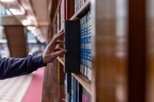 Hand selecting book from wooden library shelf. Legal research concept, attorney reference material, system study, academic knowledge and professional legislation archive.