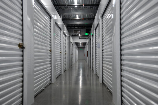 Long corridor inside a modern self storage facility. Empty storage hallway with metal roll up doors. Clean and secure indoor storage units for rent. Symmetrical storage corridor with industrial.