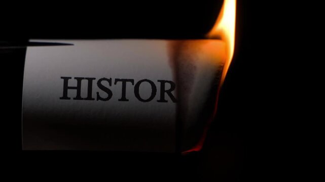 A sheet of paper with the word HISTORY burning close-up in slow motion on a black background