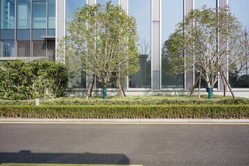 Modern office building with glass facade and landscaped green belt featuring street trees and shrubs © zhu difeng
