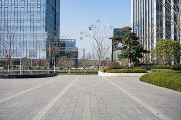 Fototapeta premium Modern urban plaza with tall glass buildings and landscaped greenery under clear sky