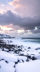 Snowy shore with rocks, the ocean, and dramatic clouds at dusk