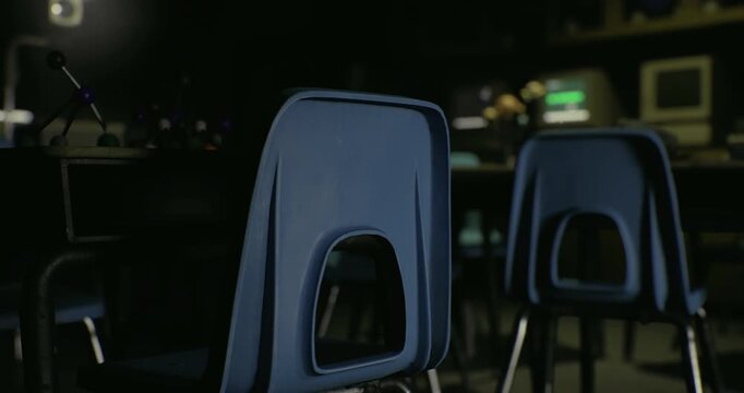 An empty classroom filled with blue chairs and soft lighting creates a quiet atmosphere, suitable for reflection or study. The surrounding space has a few scattered items on desks.