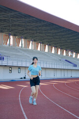 Obraz premium Young Asian woman jogging on outdoor running track at stadium, morning exercise