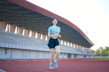Fototapeta premium Young Asian woman jogging on outdoor running track at stadium, morning exercise