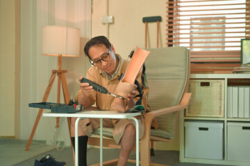 Middle aged man repairing a prosthetic leg at home with a screwdriver, focused self care and...