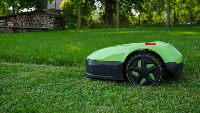 Robotic lawn mower cutting grass along the boundary wire with clear contrast between freshly mowed and unmowed areas. Smart home technology, landscaping, outdoor maintenance, and home improvement