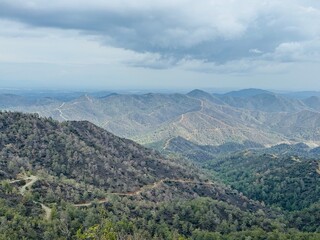 Fototapeta premium Pefkos tis Louvarous viewpoint with sweeping views of Cyprus’ forested valleys, rugged hills, and distant mountains under bright winter sunlight