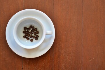 White coffee cup with roasted beans at the bottom, top view with copy space on the right