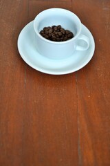 White coffee cup half filled with roasted beans, perspective view with copy space below
