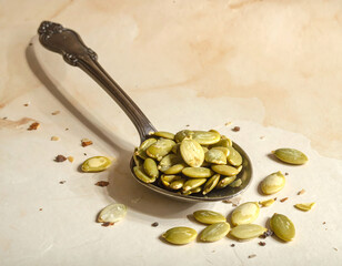 Spoonful of shelled, green pumpkin seeds on mottled paper with scattered seeds around