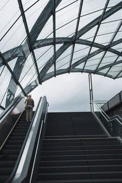 Anonymous person riding modern escalator in architecture under glass roof with interior perspective for urban travel mood and clean commercial background