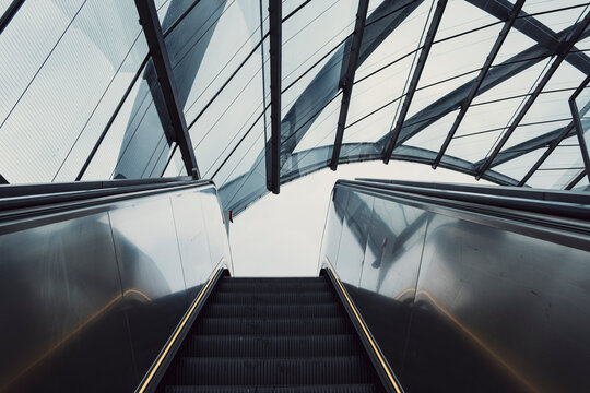 Symmetric modern escalator inside architecture below glass roof with interior perspective creating urban transport mood for travel concept and design background