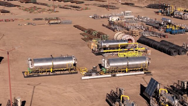 Aerial footage pulling away from an oil and gas processing facility, showing storage tanks, pipeline systems, and energy infrastructure in a desert environment.