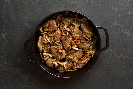 Sauteed liver with butter and onion in pan on black stone background