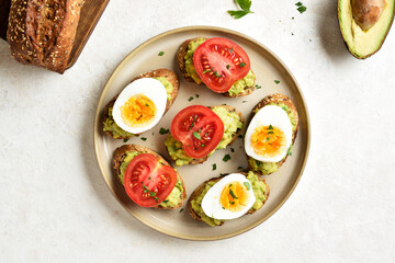 Bruschetta with mashed avocado, tomato slices and eggs