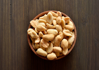 Salted roasted peanuts in bowl on brown wooden background