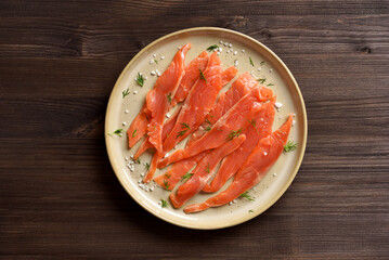 Slices of salted salmon on plate on dark wooden background