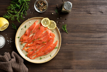 Slices of salted salmon on plate on dark wooden background