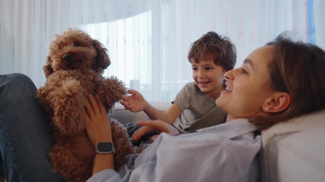 Mother and young child playing with a small dog on a cozy sofa at home. Warm family moment filled with joy, laughter, and bonding. Concept of family time, childhood happiness, pet love, and everyday