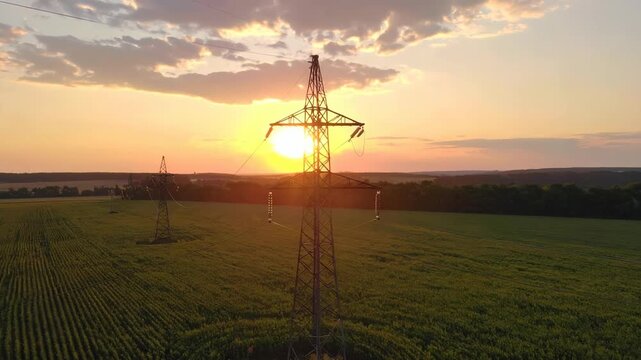 Electrical pylon silhouetted against a dramatic sunset over a cultivated field