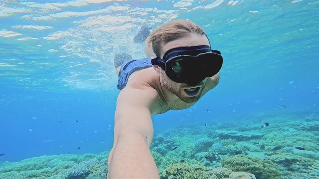 Man swimming underwater taking a selfie video ina cristal clear water