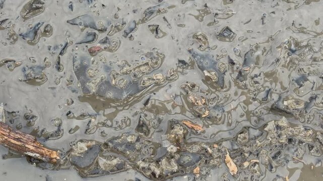 A wooden stick stirs through a mixture of crushed ice shards and murky water in a shallow puddle. This rhythmic movement causes the ice fragments to clink together while creating wet, sloshing sounds.