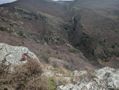 Panorama montano con una valle profonda che attraversa il paesaggio, caratterizzato da pendii ripidi e vegetazione rada tipica della stagione invernale