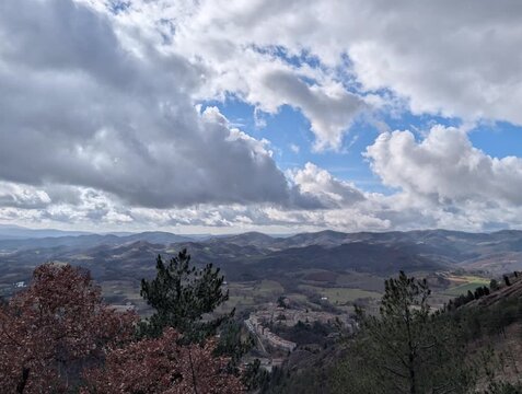 Panorama montano con una valle sinuosa che si perde tra colline e rilievi distanti. In primo piano si vedono alberi spogli e arbusti tipici della stagione invernale