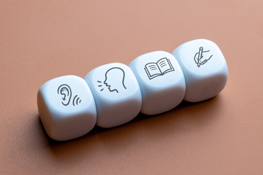 Four white cubes displaying icons for listening, speaking, reading, and writing skills. Language learning, education, communication, and literacy development concept.