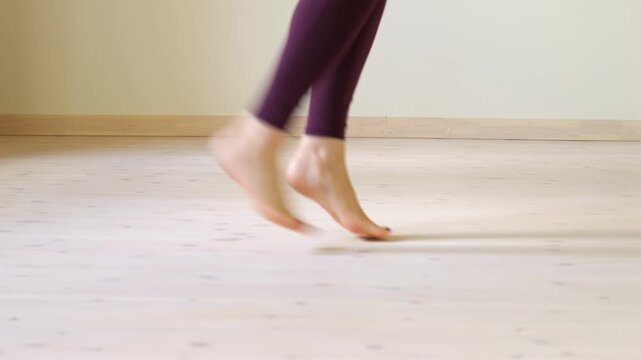 Woman is running on a wooden floor. She is barefoot. Her legs are bent. Her feet are spread apart