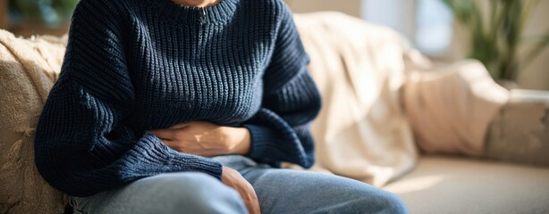 The woman clutching her abdomen on a couch, experiencing abdominal pain at home