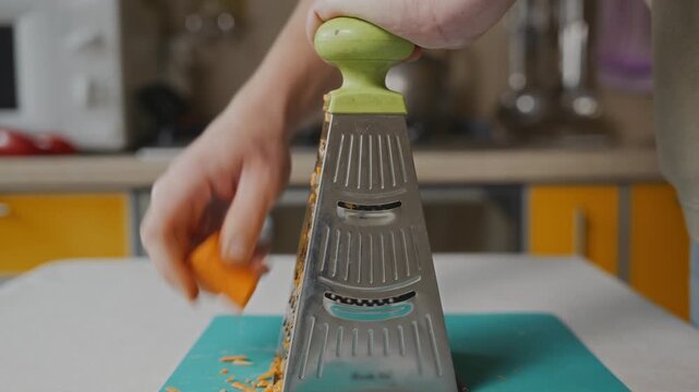 Medium shot of a man grating carrot while standing at a kitchen table. Natural home cooking process, everyday food preparation and casual lifestyle scene. High quality 4k footage