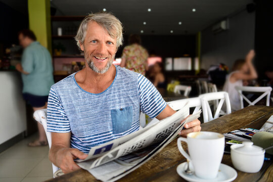 Portrait of smiling mature man sitting in a coffee shop reading newspaper