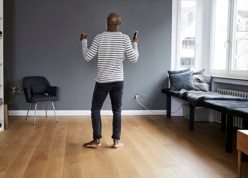Mature man dancing alone at home, holding smart phone