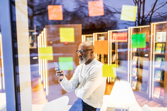Businessman behind windowpane with adhesive notes looking at cell phone