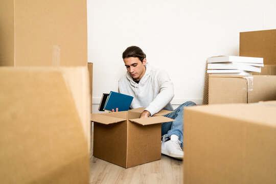Young man unpacking box while shifting in new apartment