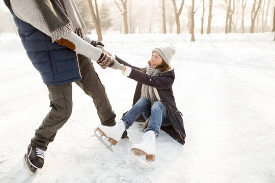 Man helping ice skating woman getting up from frozen lake