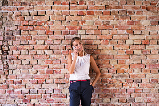 Businesswoman using cell phone at brick wall