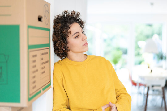 Serious woman leaning against a wall at home with cardboard boxes