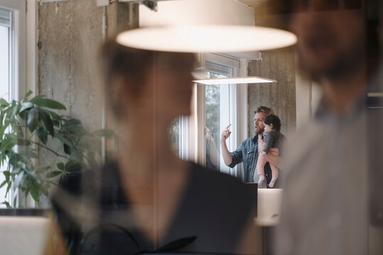 Casual businessman carrying little daughter at the window in office