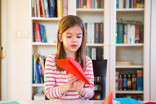 Girl tinkering paper plane on table at home