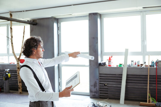 Architect with sketch book and construction plan at construction site