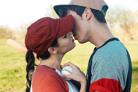 Young couple with baseball equipment kissing in park